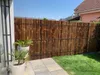 A bamboo fence in a backyard setting with potted plants and a paved walkway. Náhľad obrázku produktu