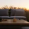 An aroma diffuser sits on a wooden coffee table on a patio at sunset, with a couch and tall grass in the background. Produktbild-Vorschau