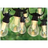 A string of outdoor lights with clear bulbs and visible filaments, set against a blurred green background of foliage. Anteprima dell’immagine prodotto
