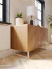 A wooden sideboard with a chevron pattern on its doors, placed on a wooden floor. A table lamp and a potted plant are on top of the sideboard. Náhľad obrázku produktu