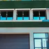 A modern building facade with windows, a garage door, and a glass entrance, partially covered by dark green privacy screens. Náhľad obrázku produktu