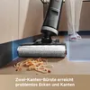 A wet and dry vacuum cleaner is shown cleaning up spilled spaghetti on a wooden floor, with a person's legs visible in the background. Produktbild-Vorschau