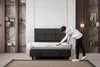 A person is unrolling a mattress in a bedroom setting. Produktbild-Vorschau