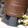 A close-up view of a brown rain barrel stand with a watering can in the background. Produktbild-Vorschau