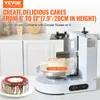 A cake decorating machine is shown in a kitchen setting, with a cake on a turntable and another cake on the side. Náhľad obrázku produktu