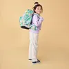 A young girl wearing a backpack and standing against a plain background. Podgląd zdjęcia produktu