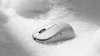 A white wireless computer mouse is placed on a surface of small white granular material, resembling snow or salt. Produktbild-Vorschau