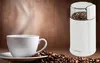 A coffee grinder and a cup of coffee are shown on a wooden surface with coffee beans scattered around. Podgląd zdjęcia produktu