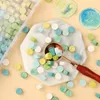 A collection of colorful wax beads scattered around a marble tray and a scoop, with a storage box of beads in the background. Náhled obrázku produktu
