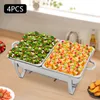 A chafing dish set with two divided compartments, one filled with salad and the other with fruit salad, on a wooden table. Additional food items are visible on plates in the foreground and background. Náhled obrázku produktu