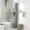 A tall, narrow gray cabinet with shelves and drawers stands in a bathroom next to a bathtub. A plant hangs in the background. Produktbild-Vorschau