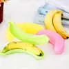 Several banana-shaped storage boxes in different colors are arranged on a white surface, with some real bananas placed inside. Produktbild-Vorschau