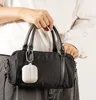 A person is holding a black handbag with a white accessory attached. Produktbild-Vorschau