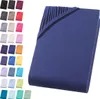 A folded dark blue fitted sheet is shown on a white background, with a collage of other colored fitted sheets arranged to the left. Produktbild-Vorschau