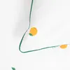 A close-up view of a white fabric with a green trim and a pattern of orange fruits and green leaves. Produktbild-Vorschau