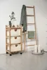A wooden laundry cart with three fabric baskets, a ladder shelf with a towel and a jacket, and two candles on a tray, placed against a white wall. Podgląd zdjęcia produktu
