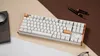 A white mechanical keyboard with wood accents is displayed on a desk with a notebook, magnifying glass, and pens. Produktbild-Vorschau