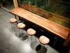 A long wooden bar table with four stools in front of a window with greenery outside. Produktbild-Vorschau