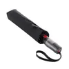 A closed black umbrella with a gray handle and a red button, lying diagonally on a white background. Produktbild-Vorschau