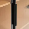 A close-up view of a black handle on a wooden cabinet door. Náhľad obrázku produktu
