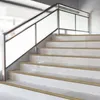 A close-up view of a modern staircase with white tiled steps and bronze-colored stair nosing, featuring a sleek metal and frosted glass railing. Podgląd zdjęcia produktu