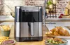 An air fryer is shown on a kitchen counter with prepared food around it. Voir les images du produit