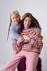 Two young girls are hugging each other, both wearing sweaters and pink pants. Produktbild-Vorschau