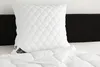 A white quilted pillow and comforter are placed on a bed with a black headboard. Produktbild-Vorschau