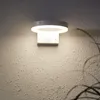 A modern white wall-mounted light fixture with a circular top and a rectangular base. Produktbild-Vorschau