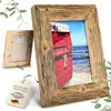 Two wooden picture frames, one with a photo of a red boat on a beach, are displayed against a white background, with a tag attached to the front frame. Produktbild-Vorschau