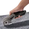 A hand is holding a cordless electric scissors and cutting a gray carpet. Náhled obrázku produktu
