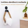 A toilet paper holder made of natural jute rope is shown hanging on a white wall, with a roll of toilet paper on it. A small plant in a brown bottle is visible on a wooden shelf in the background. Anteprima dell’immagine prodotto