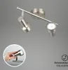 A close-up studio shot of a silver LED ceiling light with two adjustable spotlights against a plain gray background. A circular inset shows a hand adjusting one of the spotlights. Produktbild-Vorschau