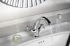 A close-up shot of a chrome faucet with water running into a white sink. There are also a few cosmetic items on the sink. Anteprima dell’immagine prodotto
