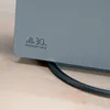 A close-up view of a gray PlayStation console with a 30th Anniversary logo embossed on it, resting on a wooden surface. Produktbild-Vorschau