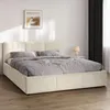 A beige upholstered bed with a headboard and storage drawers, set in a bedroom with a framed picture on the wall and dark curtains.