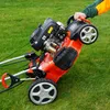 A person is tilting a lawnmower on a grassy lawn. Produktbild-Vorschau