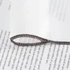 A close-up of a brown fabric choker necklace lying on a white background with text from a book visible underneath. Produktbild-Vorschau