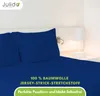 A close-up view of a navy blue bed sheet and pillowcase set on a bed, with a bedside lamp and wall light visible in the background. Produktbild-Vorschau