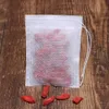 A white tea bag filled with red goji berries sits on a wooden surface, with a few loose goji berries scattered around it. Produktbild-Vorschau