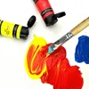 Close-up of art supplies including paint tubes and a paintbrush on a white surface with paint splatters. Produktbild-Vorschau
