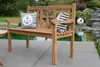 A wooden bench with nautical-themed pillows sits on a patio next to a pond. Produktbild-Vorschau