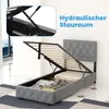 A bed frame with its storage compartment open, revealing a mattress and some folded clothes. The bed is upholstered in gray fabric and has a diamond-stitched headboard. A close-up inset shows the hydraulic lift mechanism. Náhled obrázku produktu