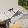 An outdoor sink mounted on a wall next to a marble countertop, with a tiled patio and grass in the background. Produktbild-Vorschau