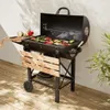 A charcoal grill with vegetables on it, placed on a wooden deck next to a wall. Produktbild-Vorschau