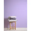 Three pillows stacked on a wooden stool against a solid light purple wall. Produktbild-Vorschau