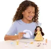 A young girl is playing with a doll and accessories on a white table. Produktbild-Vorschau