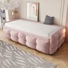 A pink sofa bed with a white mattress is shown in a bedroom setting, with a rug on the floor and a framed picture on the wall. Produktbild-Vorschau