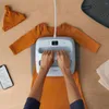 A person is using a Cricut heat press to apply a design to a baby onesie. Produktbild-Vorschau