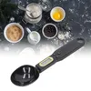 A digital measuring spoon scale is shown in the foreground, with various baking ingredients like flour, brown sugar, chocolate chips, and an egg in the background. Náhľad obrázku produktu